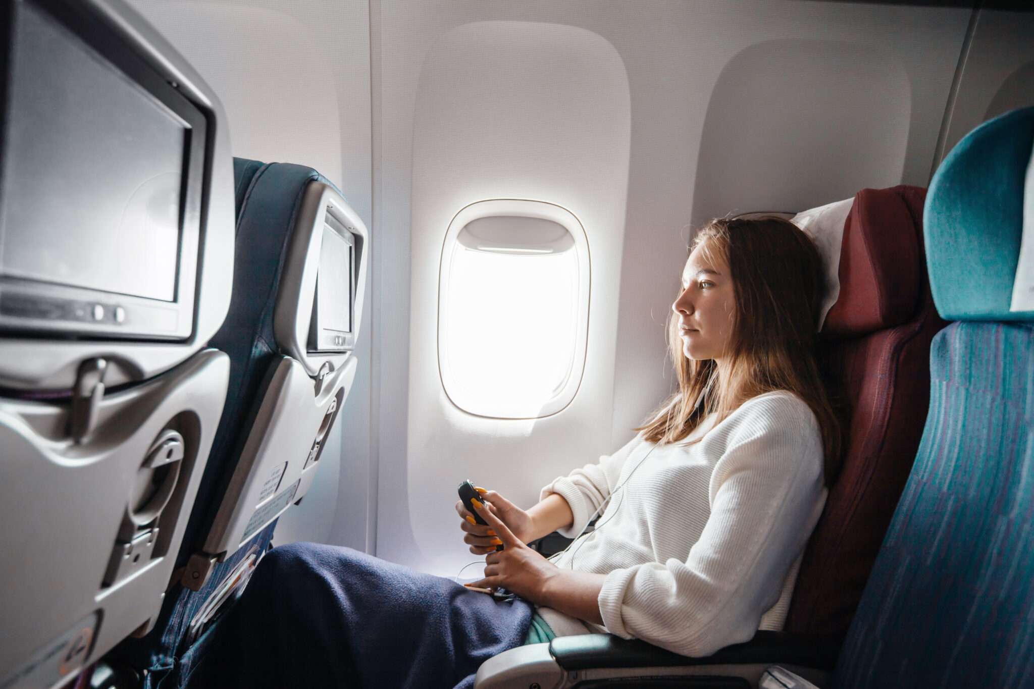 フランスへ向かう飛行機の中で座って携帯電話を見ている女性。