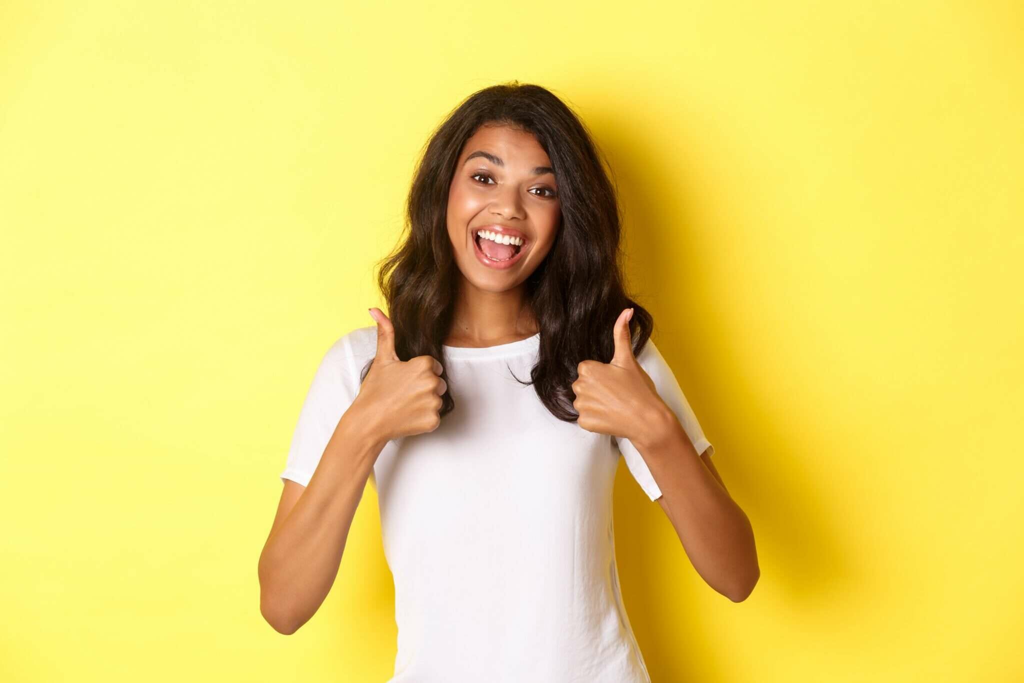 フランスで黄色の背景に親指を立てる若い女性。