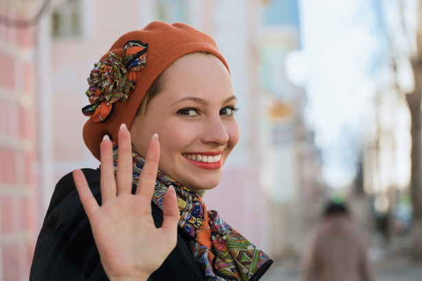 フランスでスカーフと帽子をかぶった女性が手を振っている。