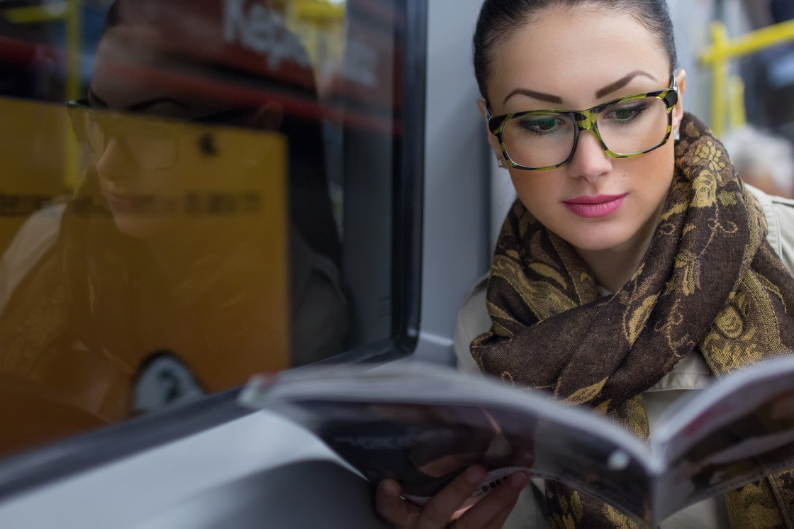 フランスの電車の中で眼鏡をかけた女性が本を読んでいる。