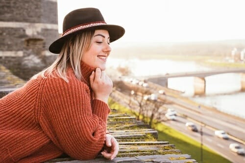 フランスの川の近くで、帽子をかぶった女性が壁にもたれかかっている。