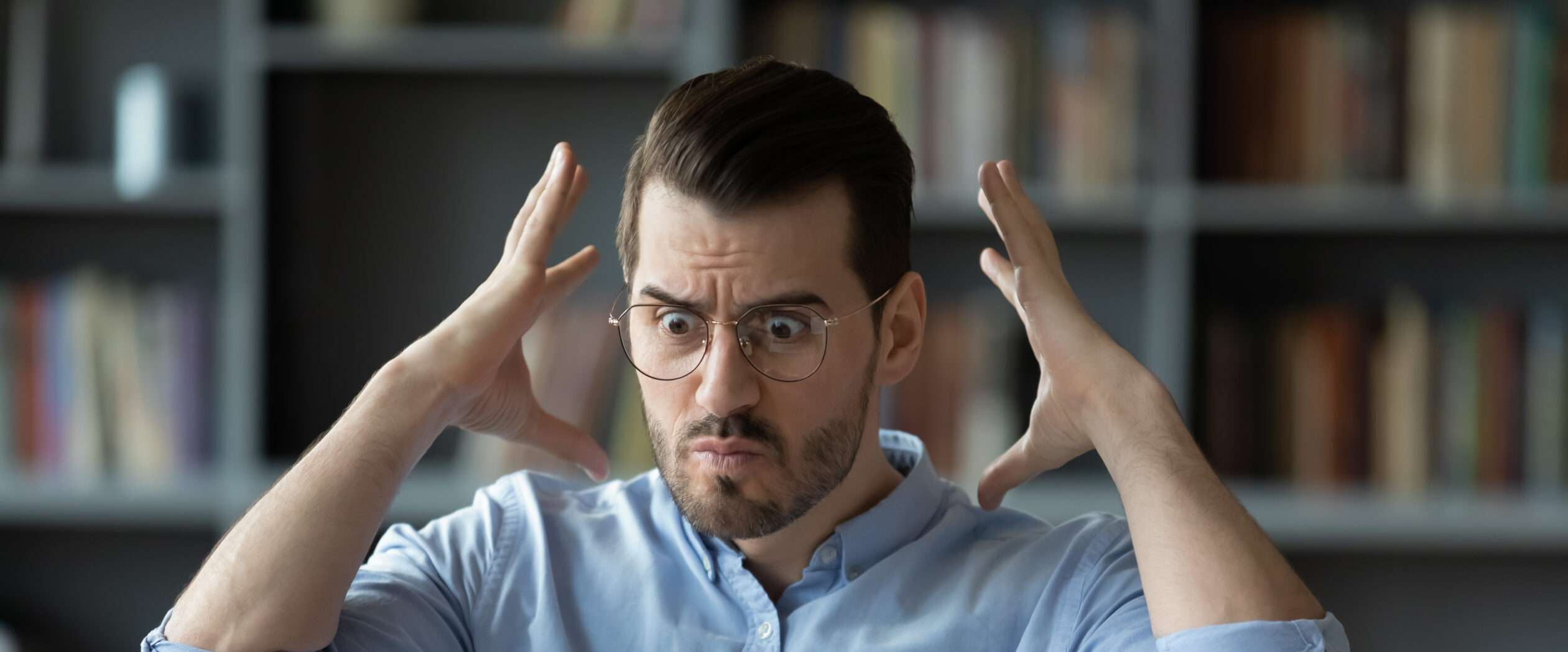 フランスの本棚の前で眼鏡をかけた男性が両手を上げている。