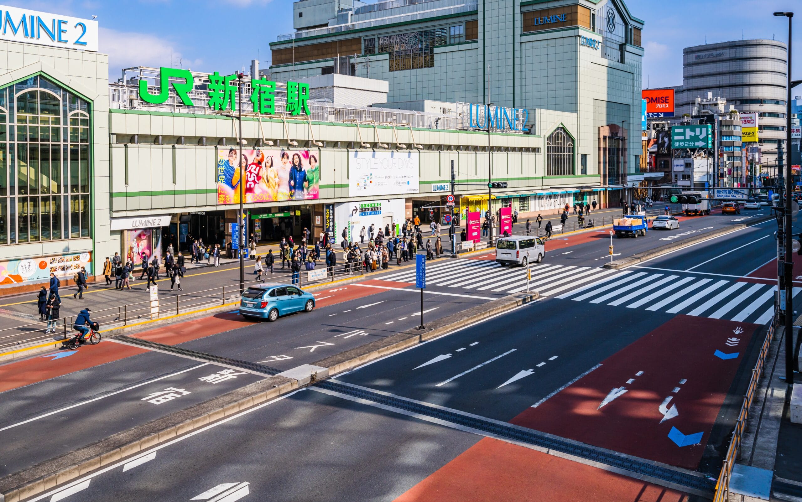 晴れた日の東京の新宿駅の都市のストリートビュー。歩行者、車両、周囲の建物が見える。近くのフランス語教室マンツーマンでは、新宿の賑やかなエネルギーの中で、個人に合わせたフランス語レッスンを提供しています。.