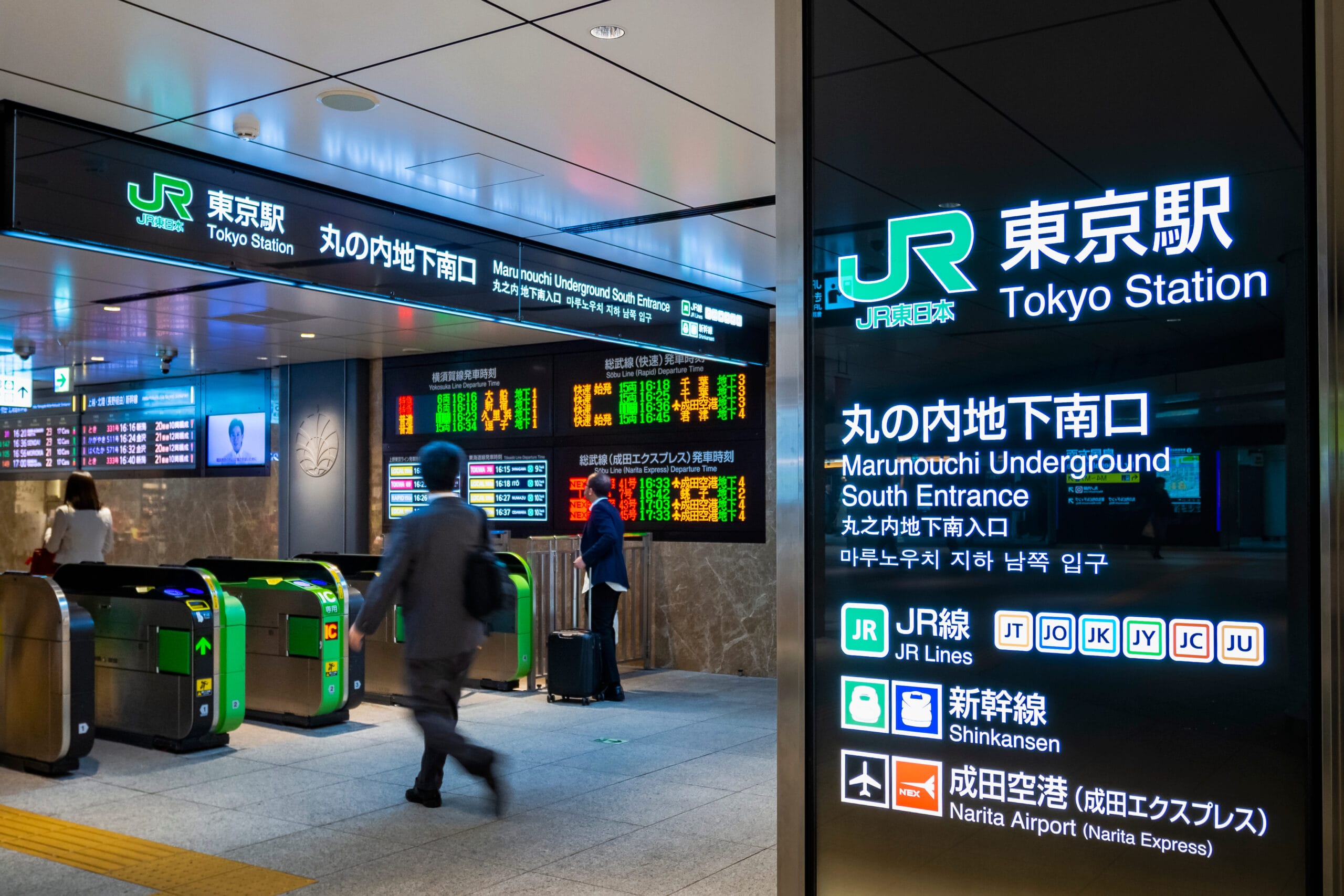 さまざまな路線や目的地を示す標識に囲まれた東京駅の入り口を人々が歩いていますが、近くのカフェでは学びたい人のためにフランス語教室マンツーマンのレッスンが提供されています。.